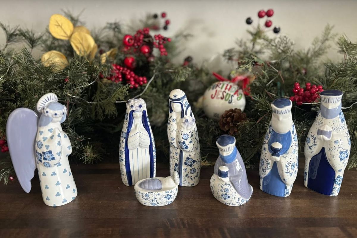 A blue and white ceramic nativity set displayed on greenery and berries